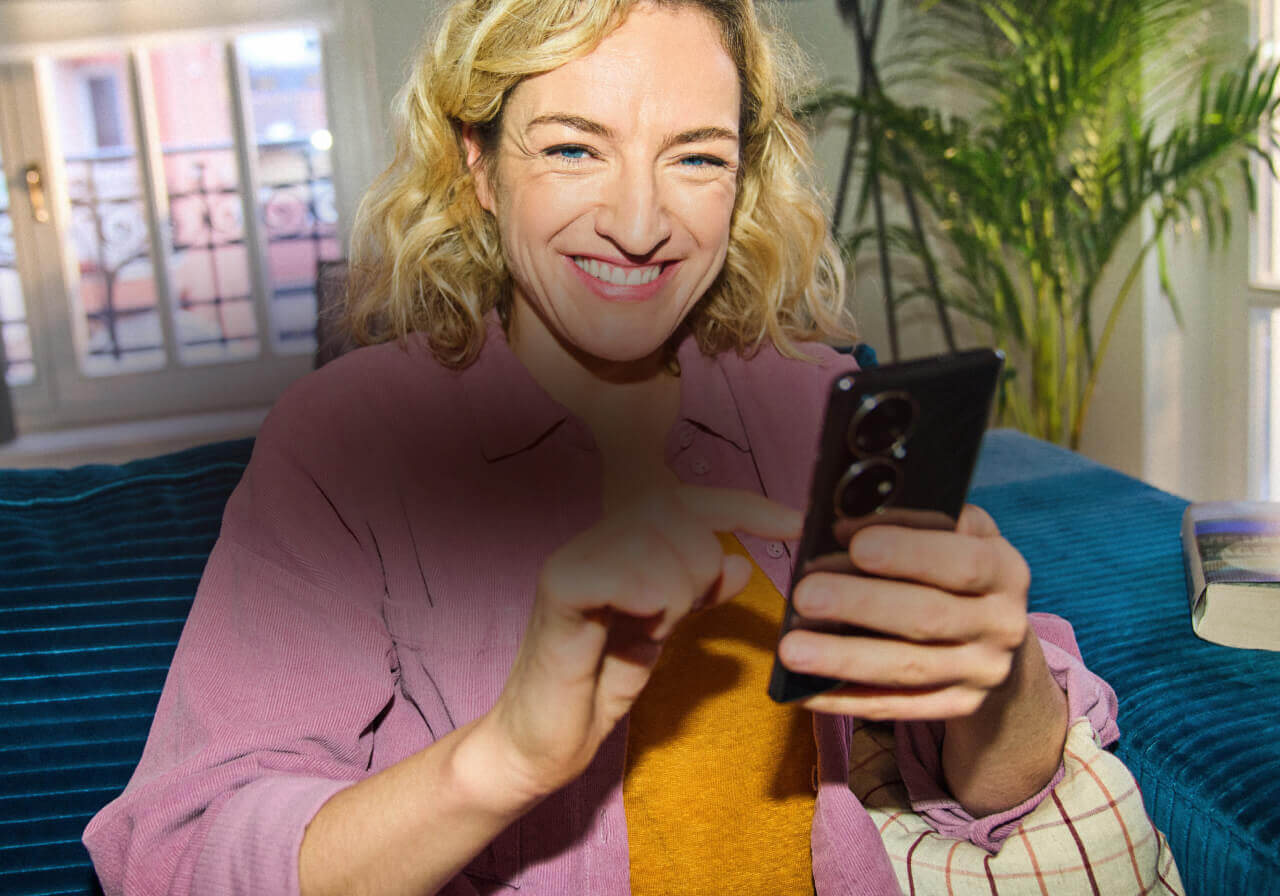 Eine Frau schaut in die Kamera und lächelt, in ihrer Hand ist ein Smartphone