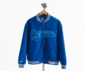 A blue Supreme Mitchell & Ness Doughboy Twill Varsity Jacket hangs from a hanger against a white background.
