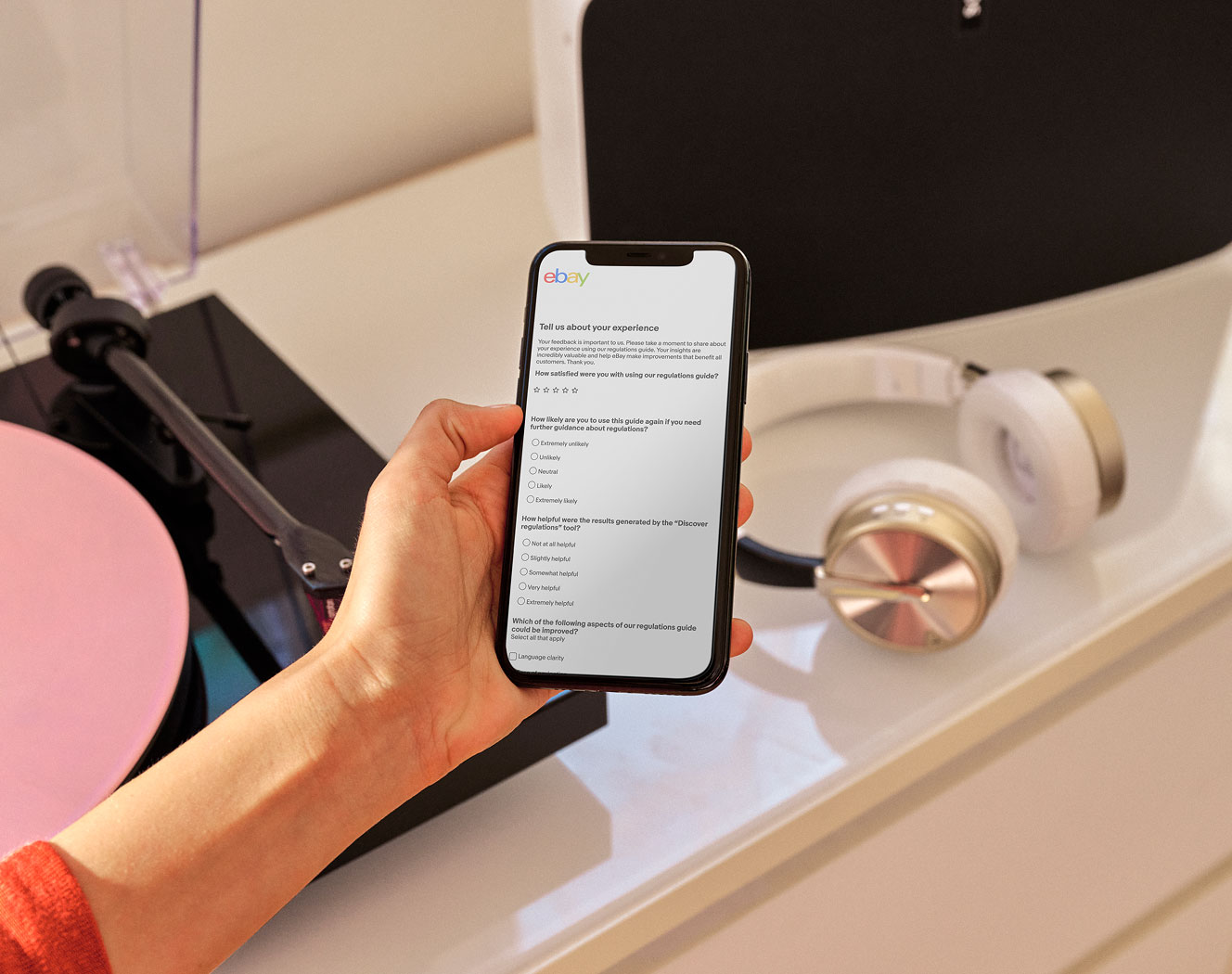 Hand holding smartphone with survey displayed, above turntable with pink vinyl and white-gold headphones.