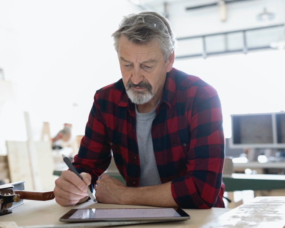 A man sitting at a table, writing on a tablet with a pen.