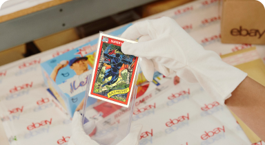 A person wearing white gloves packs a trading card into the eBay standard envelope.