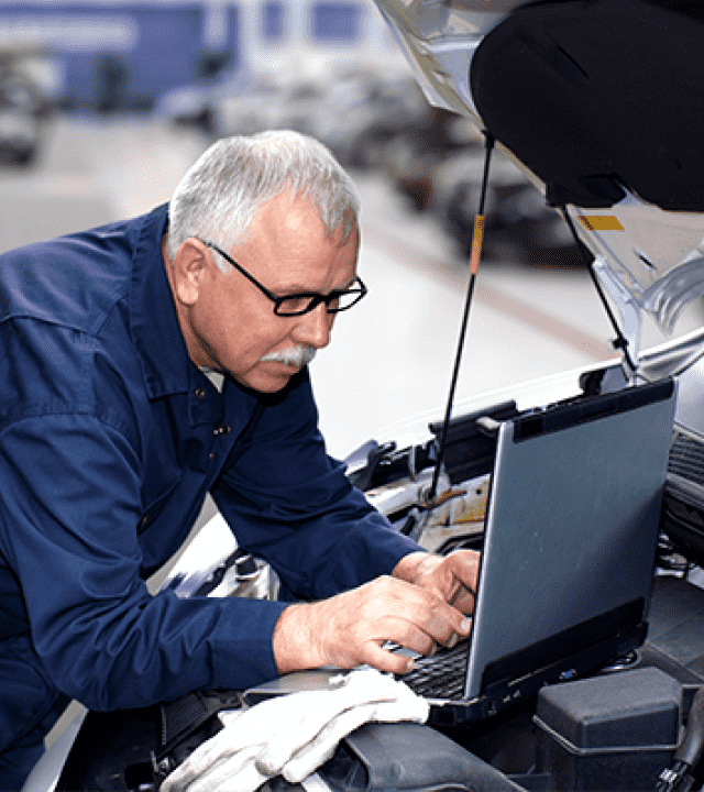 A mechanic in dark blue overall is examing the engine of a car.