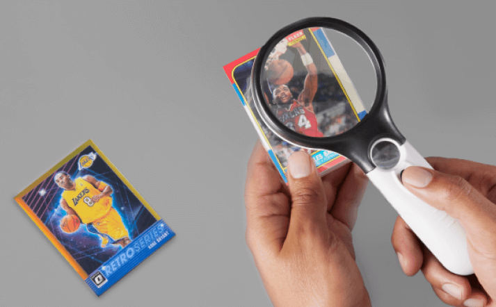 A basketball card under a magnifying glass along with another card on a grey background.