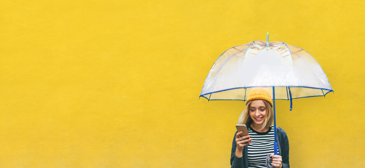 Frau schaut mit Regenschirm auf ihr Smartphone