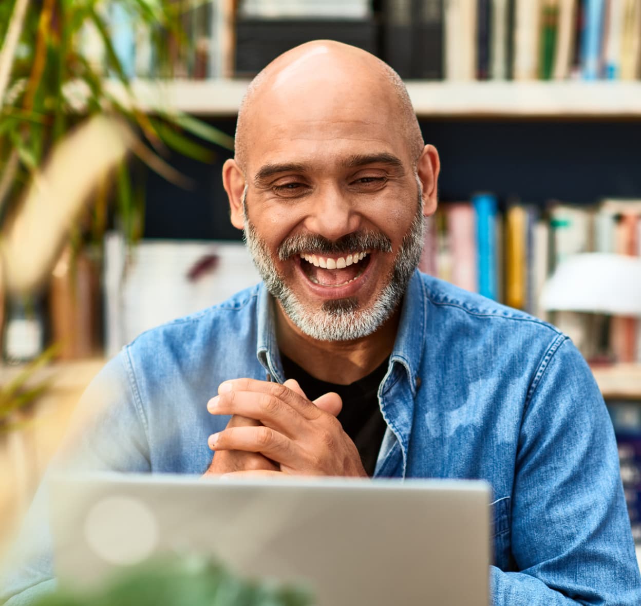 An image of a man smiling and clapping his hands looking at a laptop. 