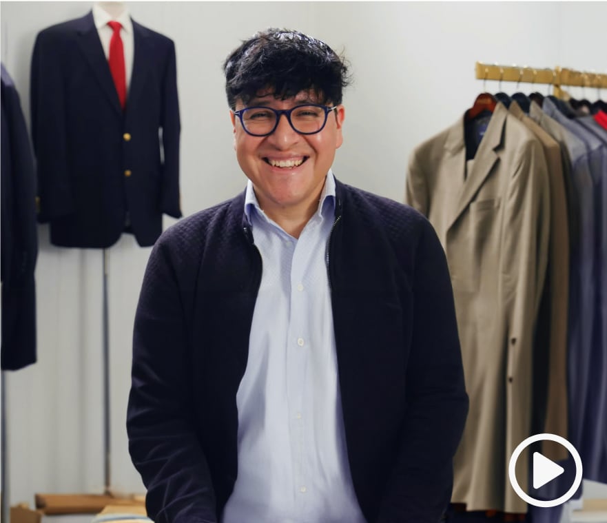 Seller Alex Carrera smiling at the camera with a rack of blazers and coats and a suited up mannequin behind him.