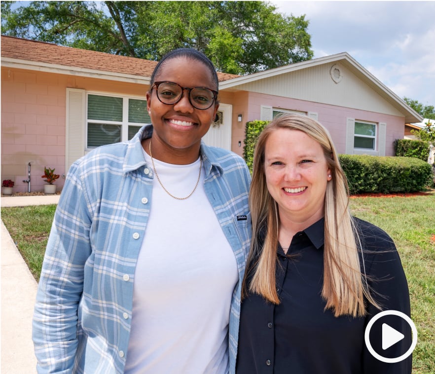 Sellers Alicia Wright and Heather Hardy smiling at the camera with a driveway and a house behind them.