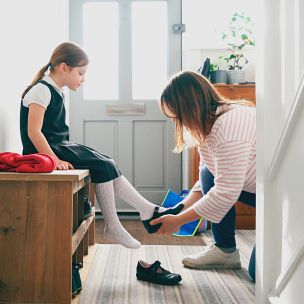 Girl in her school uniform is getting her shoes put on by her mother.