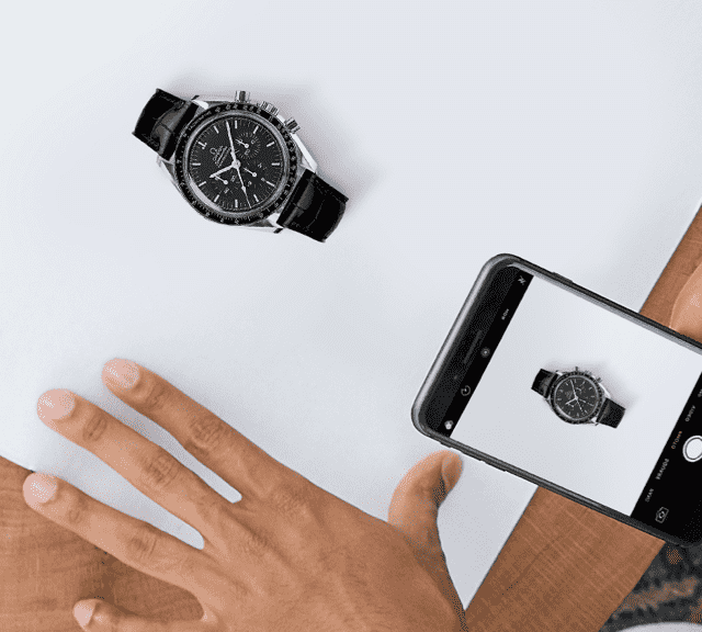 A person taking a picture of an OMEGA watch in a box.