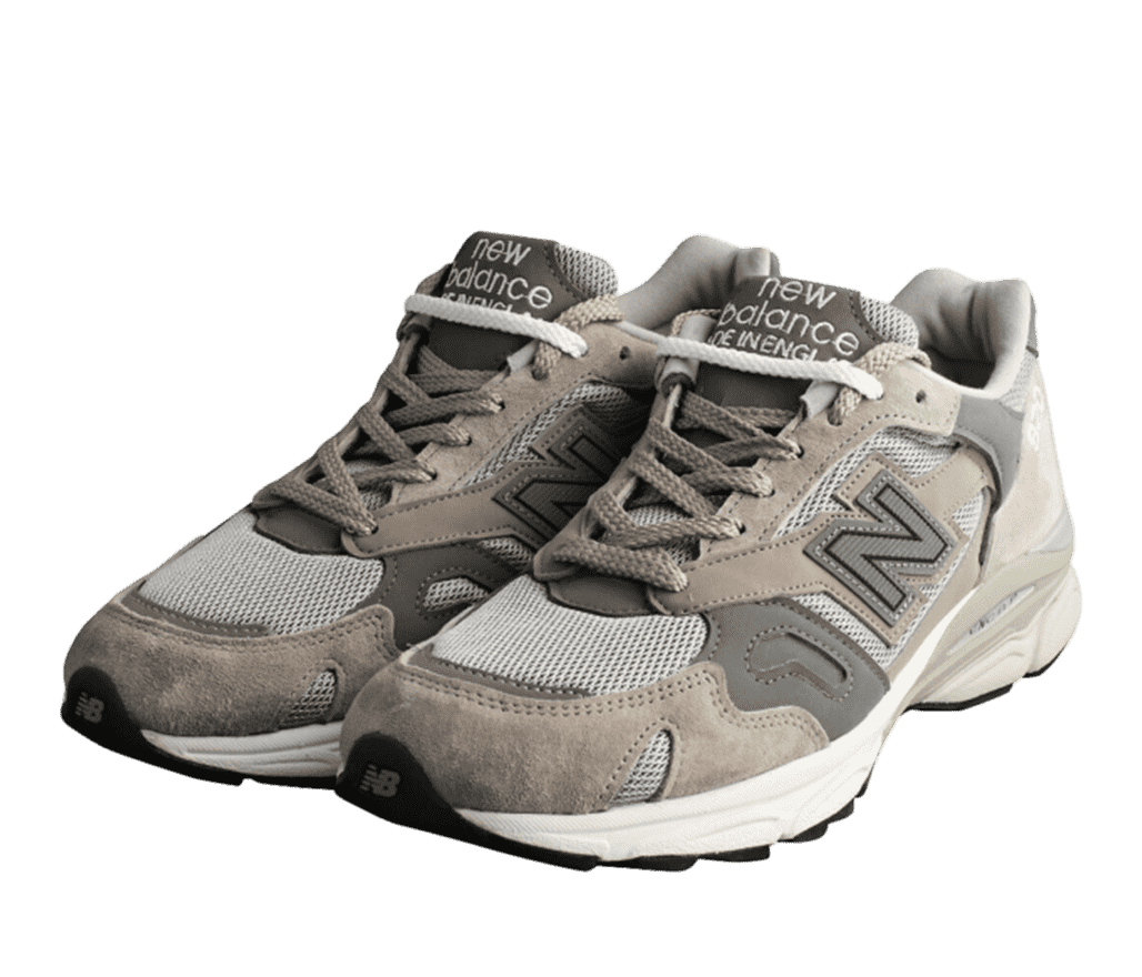 Front right angled view of a pair of two-toned New Balance brown and grey sneakers. The top of the toe and down the sides beneath the material is a white mesh material. New Balance Made in England is on the tongue.
