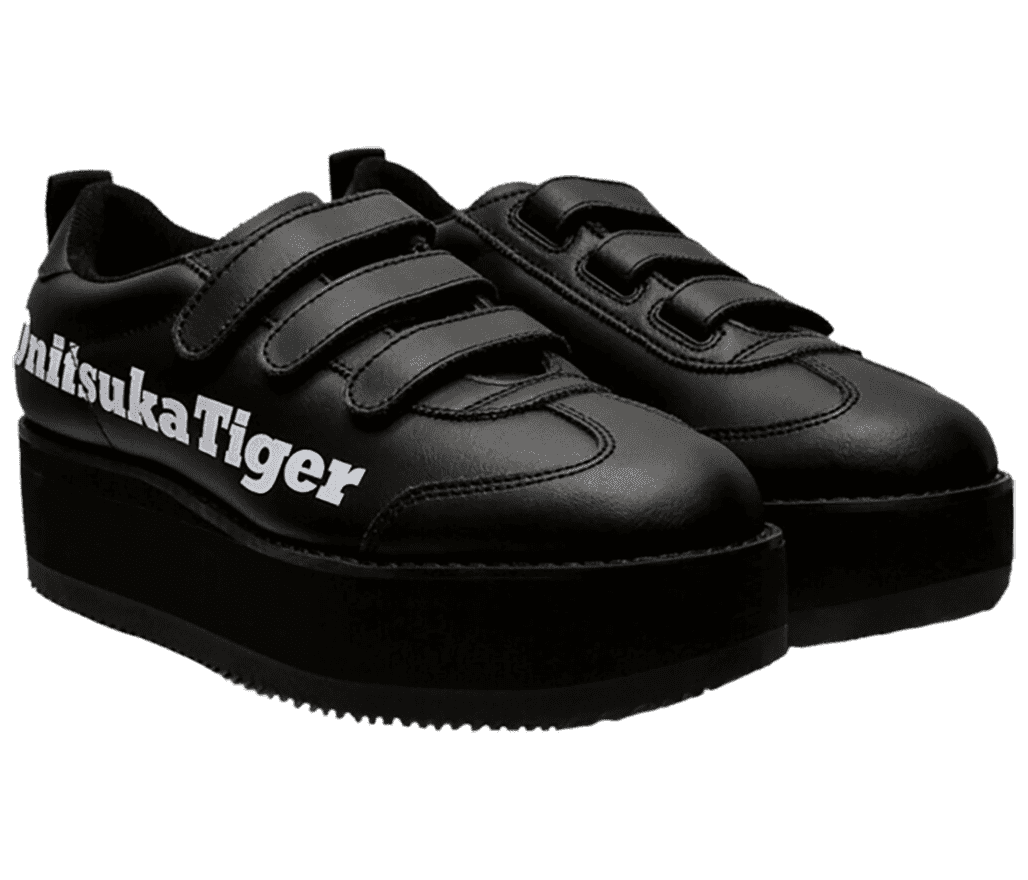 A pair of Onitsuka Tiger Delegation Chunk shoes featuring a belt with hook-and-loop velcro fasteners and a platform sole. They are all-black with “Onitsuka Tiger” printed in white block letters on the lateral side.