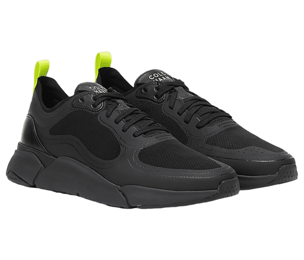 A pair of Cole Haan Grandsport trainers in all-black with raised heels and lime-green heel loops.