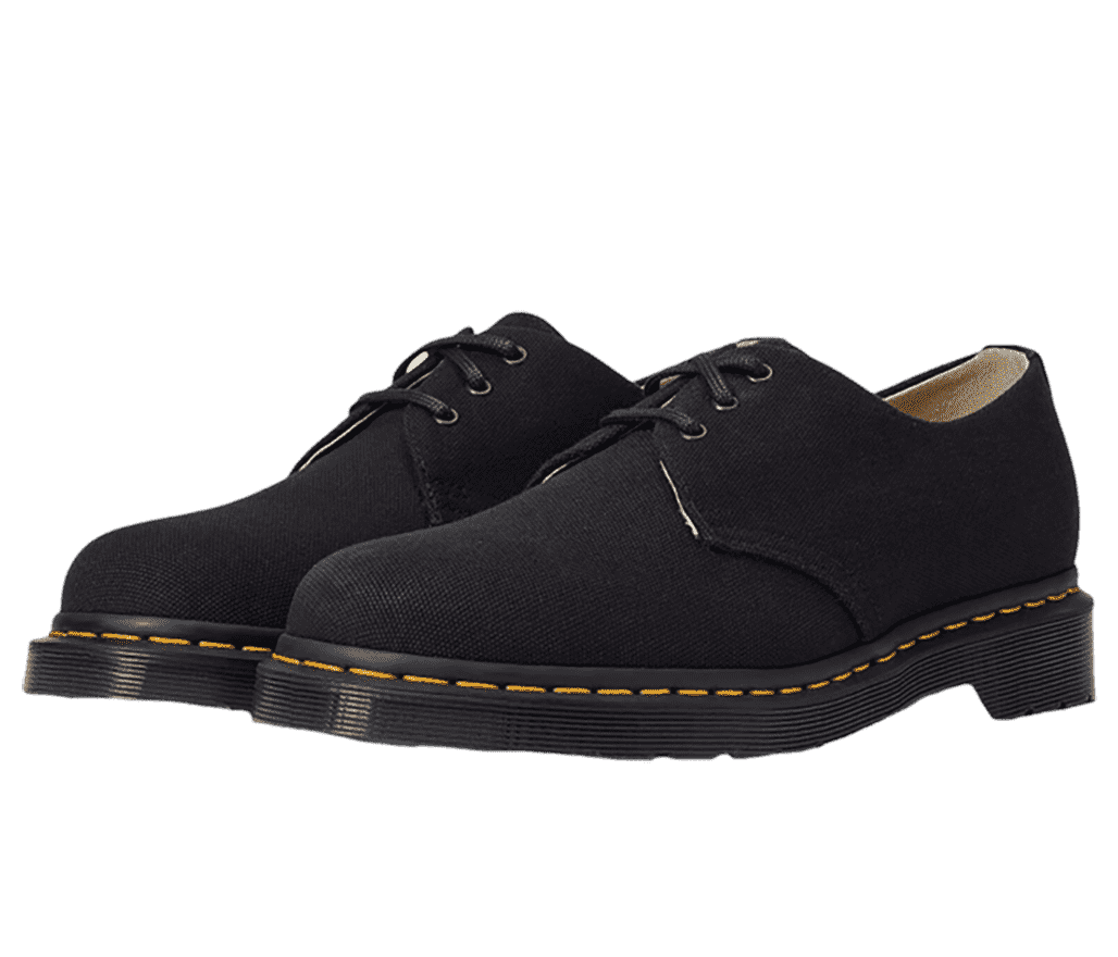 A pair of Dr. Martens 1461 low-cut shoes in all-black and the signature yellow stitching running around the top of the soles.