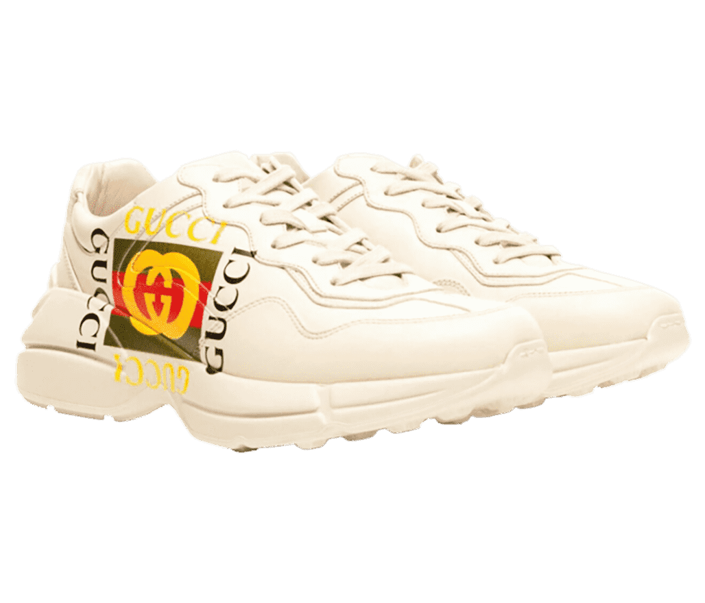 A pair of Gucci Rhyton sneakers in off-white paneled leather uppers, featuring classic red, green, yellow and black Gucci logos on the lateral sides.