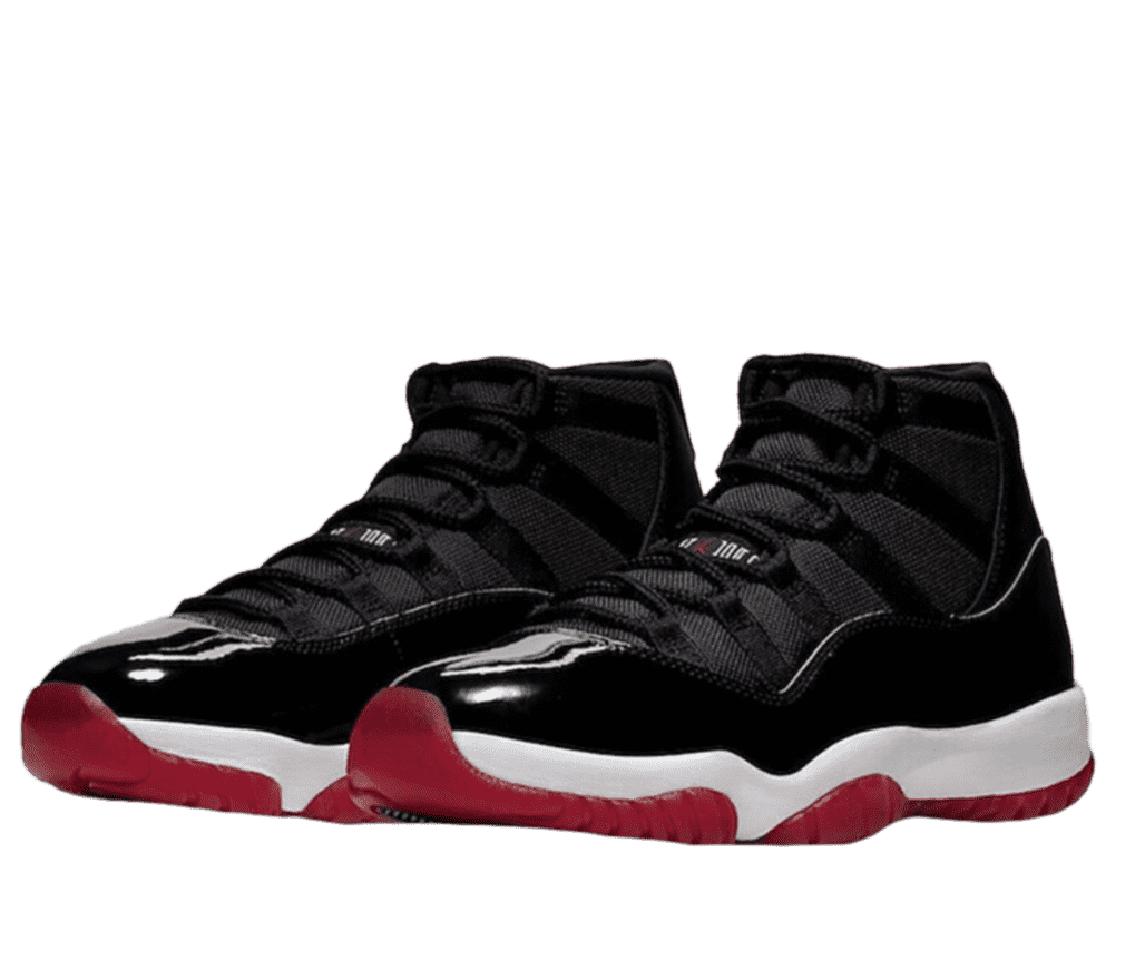 A pair of black, white, and red Air Jordan 11s. The bottom of the sole is red with white on the sides. The rest of the shoe is black with a small Air Jordan logo on the tongue in red and white.