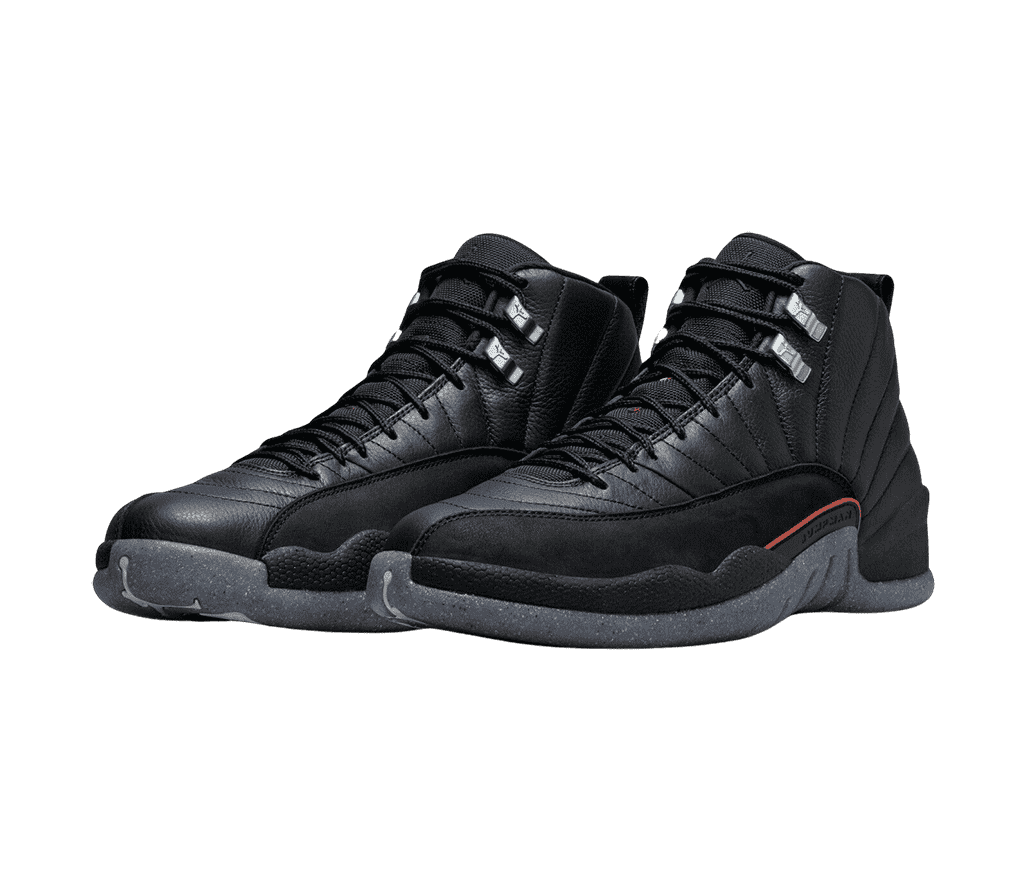 An all-black leather pair of AJ12 Retro sneakers with suede mudguards, speckled navy soles, a red accent on the lateral side, and gray lace locks.