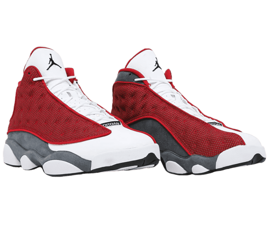 A pair of AJ13 “Red Flint” sneakers with dark gray quarters, white tongue and toeboxes, red suede vamps with circular embroidery, black outsoles, and a black Jordan logo.