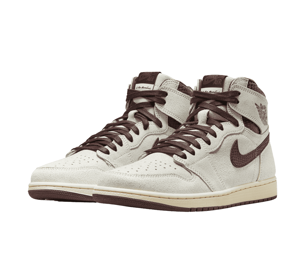 A cream suede pair of AJ1 “A Ma Maniére” sneakers. The collar and Swoosh are in a brown snakeskin. The midsole has a yellowish tint and the outsole and laces are also brown.