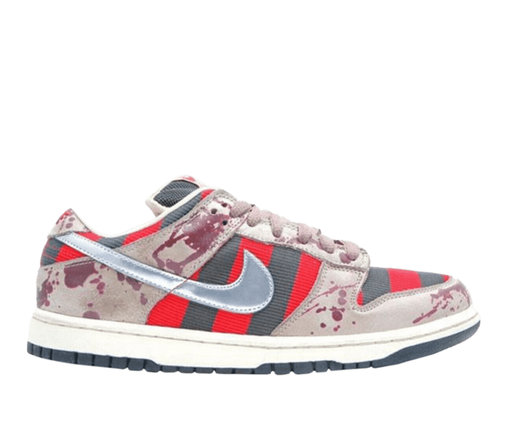 A side shot of a Nike SB sneaker. The shoe is mostly cream-colored, with maroon paint-splattered accents throughtout the shoe. The sides and front of the shoe are red and gray alternating vertical stripes. The Nike logo on the side is a metallic, shiny gray.