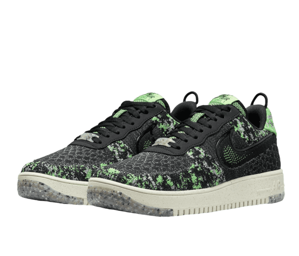 A pair of Nike sneakers with various colours and patterns. The sole is white, with a section grey speckled section on the front. The upper of the shoe is primarily black and light green with a pattern reminiscent of a digital camoflauge. Laces and inner of the shoe are black.