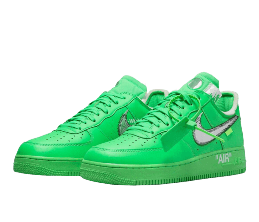 A pair of Nike Air Force 1s in bright green. The Nike swoosh is metallic silver with zig-zag stitches along the edges. 'AIR' is written on the green sole in capital letters and quotations. A matching green zip-tie tag is attached to the laces on the front shoe.