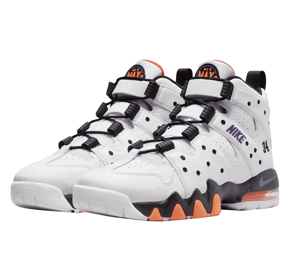 A pair of primarily white Nike Air Max 2 CB 94s. The shoe is all leather with strap-like designs and perforations across the side. 'Nike' is embroidered in purple across the side, with '34' in black near the heel. The sole is black with orange highlights, a purple Nike swoosh, and a clear Nike Air bag, with orange inside. The shoe is cut high with a black and orange interior and a large orange and purple Air Max logo on the tongue.