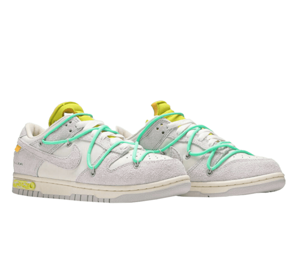 A side, angled view of the Nike Dunk Low x Off-White “The 50”. This edgy colorway comes in an off-white base and a light gray suede overlay. The Nike swoosh on the sides are in a matching gray suede. Embellishing the shoe is a teal overlace, an orange tag at the lateral side of the swoosh, and a lime green tongue and rubber plaque near the heel of the sole, showcasing the shoe’s lot number.