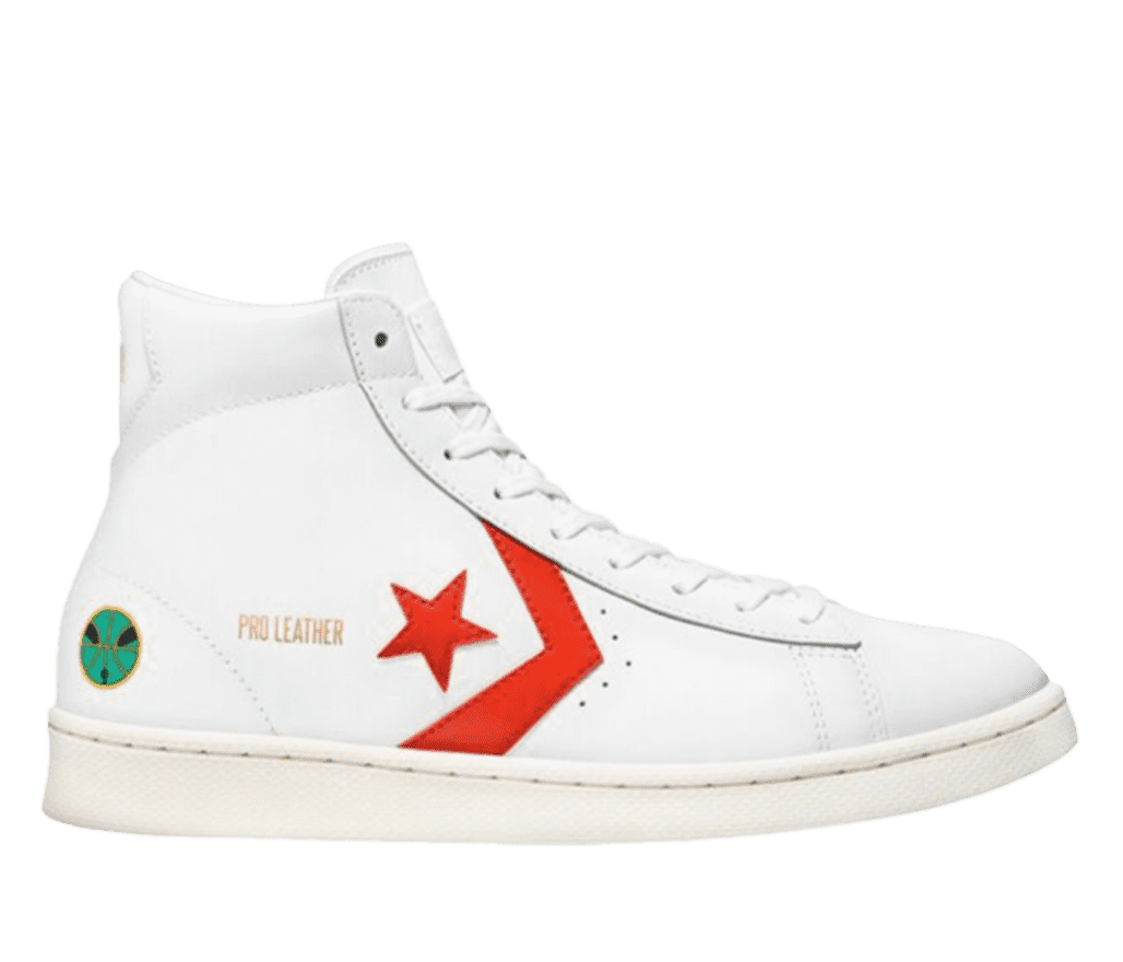A side shot of a white Converse shoe. While mostly white, the side of the shoe has an orange Converse 'star and arrow' logo. Beside the logo, the words 'Pro Leather' are written in gold. Near the back of the shoe is a small green and black basketball thats outlined in gold.