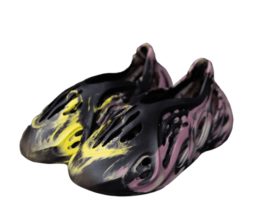 A pair of black Yeezy clogs with a scooped front resembling a train. The front of the shoe features a yellow paint-splash design, with several tall verticlal holes. The sides feature a pink paint-splash design, with circular holes across the width of the shoe.